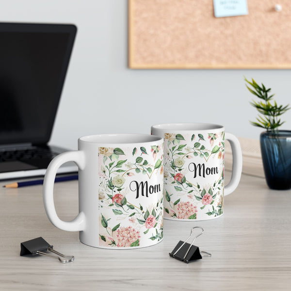 Two mugs with floral designs and 'Mom' text on a desk with office items.