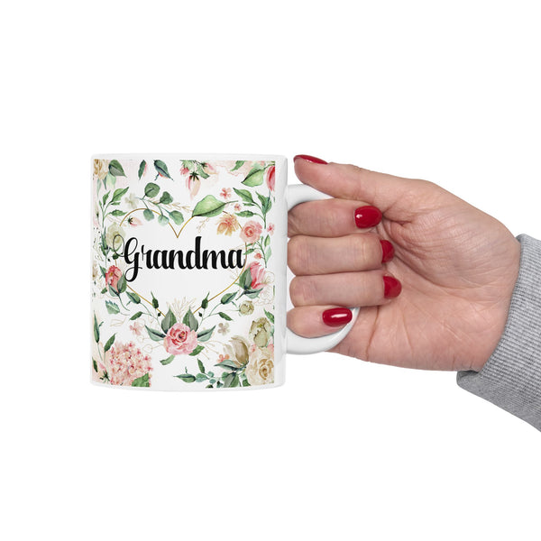 Mug with floral design and 'Grandma' text held by a hand with red nail polish on a white background