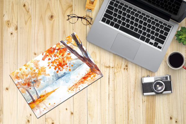 Laptop on a wooden desk with a scenic mouse pad, camera, and coffee cup.