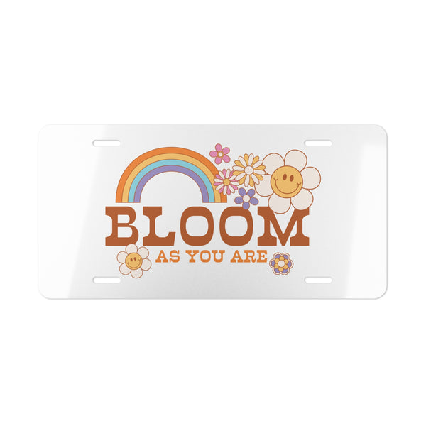 Decorative license plate with rainbow, flowers, and 'Bloom as You Are' text on a white background