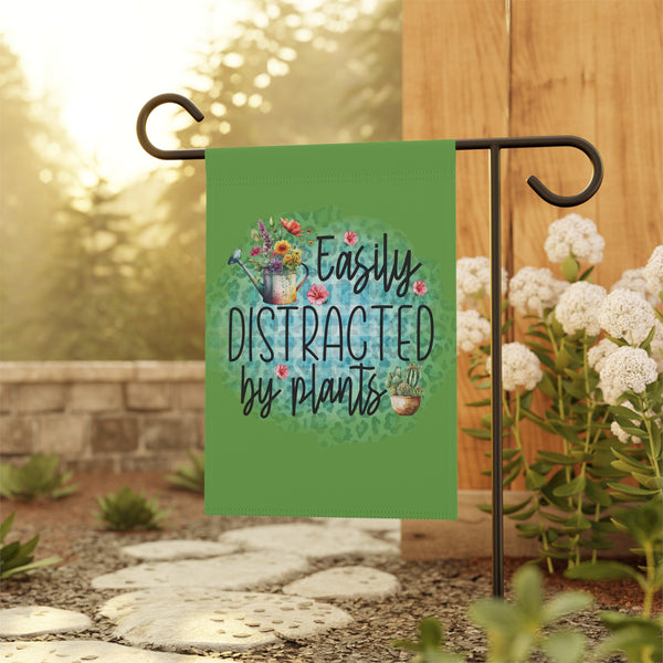 Garden flag with 'Easily Distracted by Plants' text and floral design on a stand outdoors.