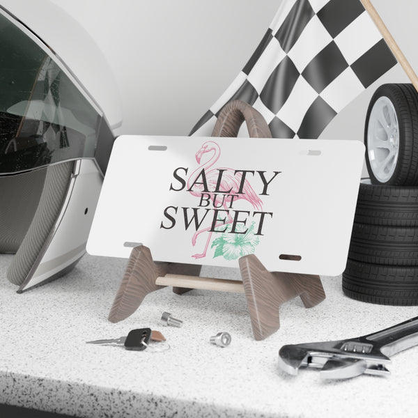 License plate with 'Salty But Sweet' text on a stand, surrounded by car parts and tools.
