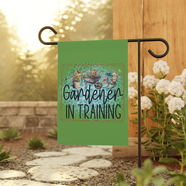 Garden flag with 'Gardener in Training' text on a stand with flowers and stones in the background
