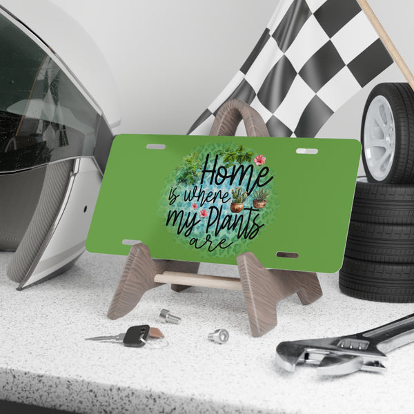 Green license plate with 'Home is where my plants are' text on a stand, surrounded by car parts and tools.