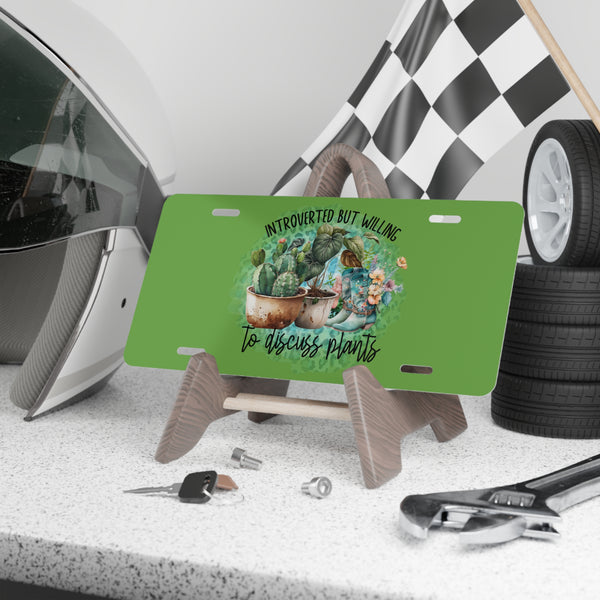 Green license plate with cactus design and text, placed on a stand with tools and helmet in the background.