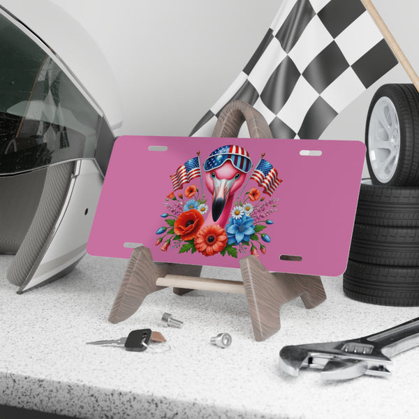 Pink license plate with a flamingo design featuring American flags, flowers, and sunglasses on a stand.
