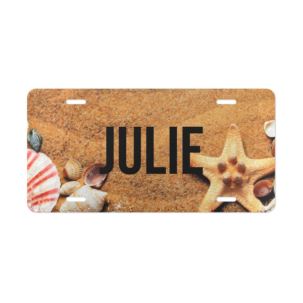 License plate with 'JULIE' text and beach-themed design featuring shells and a starfish on a sand background.
