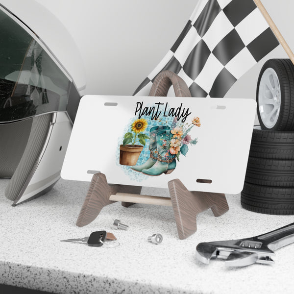 License plate with 'Plant Lady' design on a stand, surrounded by car parts and tools.