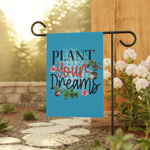 Garden flag with 'Plant Your Dreams' text and plants on a stand outdoors.