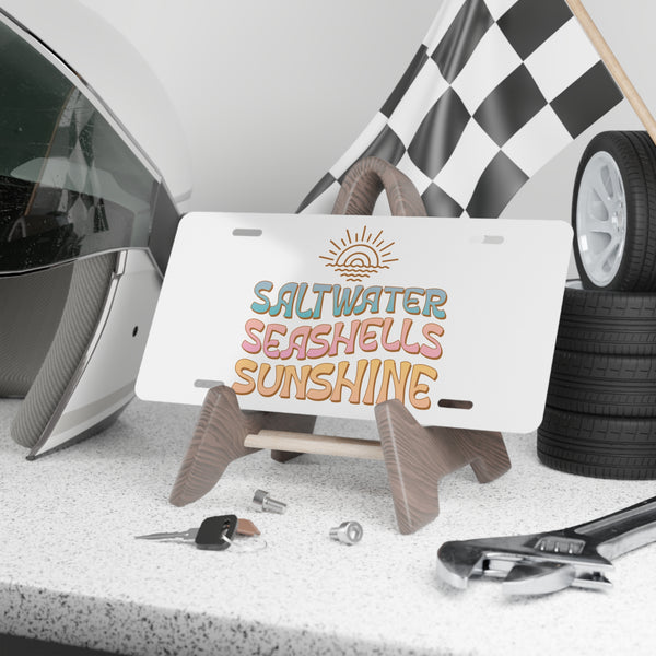 License plate with 'Saltwater Seashells Sunshine' text, helmet, tools, and checkered flag in the background