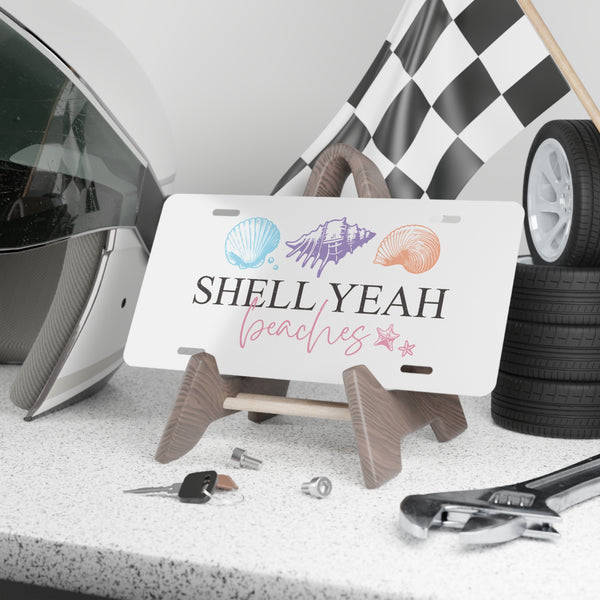 License plate with 'Shell Yeah Beaches' design on a stand, surrounded by car parts and tools.
