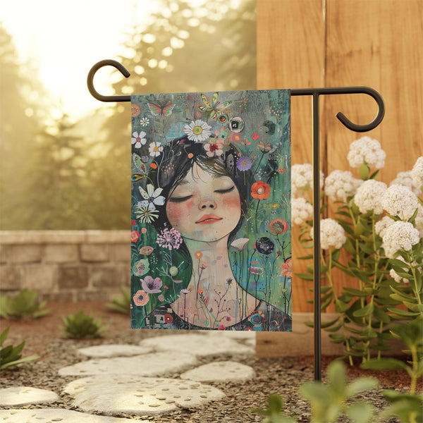 Decorative garden flag with a floral design featuring a woman's face, hanging outdoors.