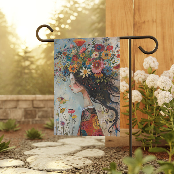 Decorative garden flag with a colorful design of a woman with flowers in her hair, displayed outdoors.