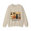 Beige sweatshirt with Halloween-themed design featuring a black cat, pumpkin, and witch on a white background.