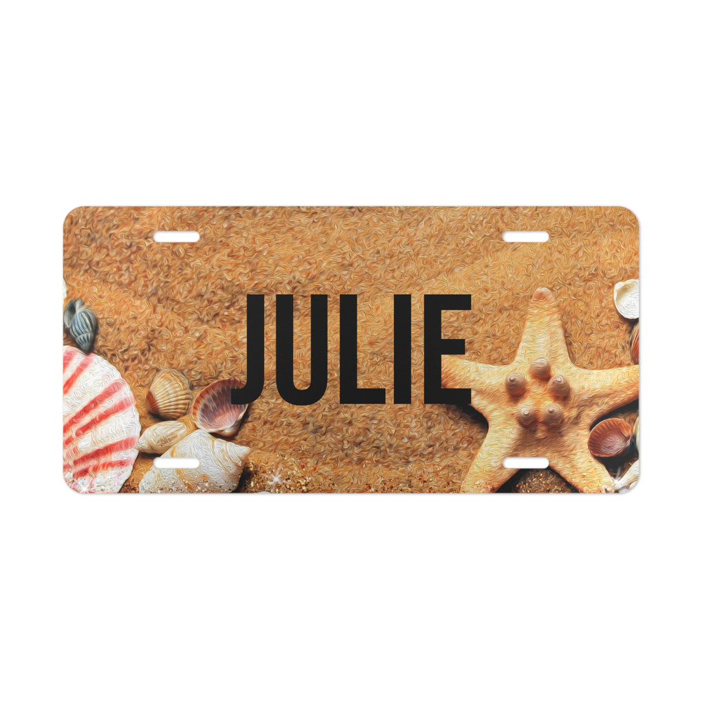 License plate with 'JULIE' text and beach-themed design featuring shells and a starfish on a sand background.